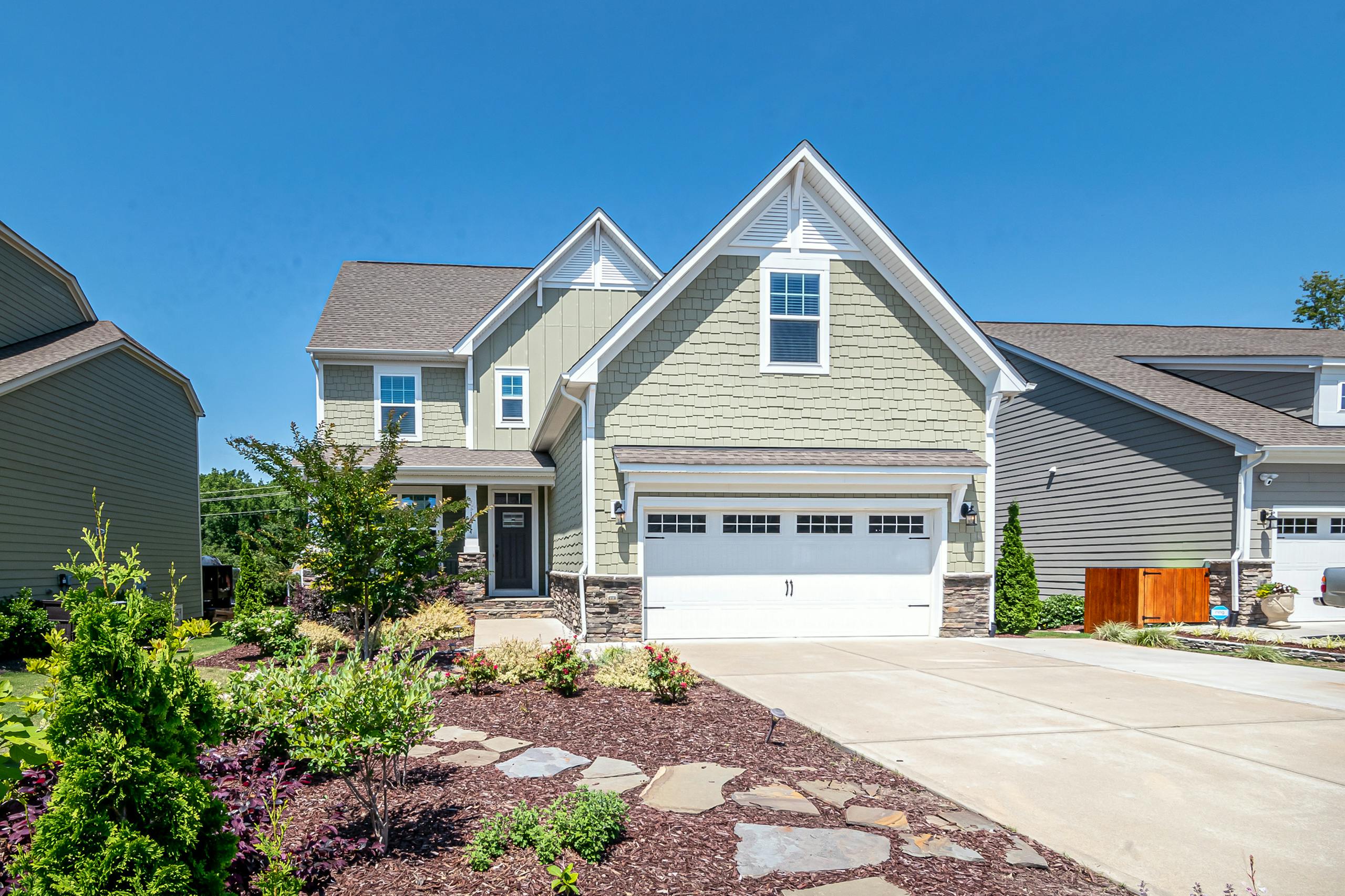 Charming suburban house with green facade, garage, and landscaped yard on a clear day.