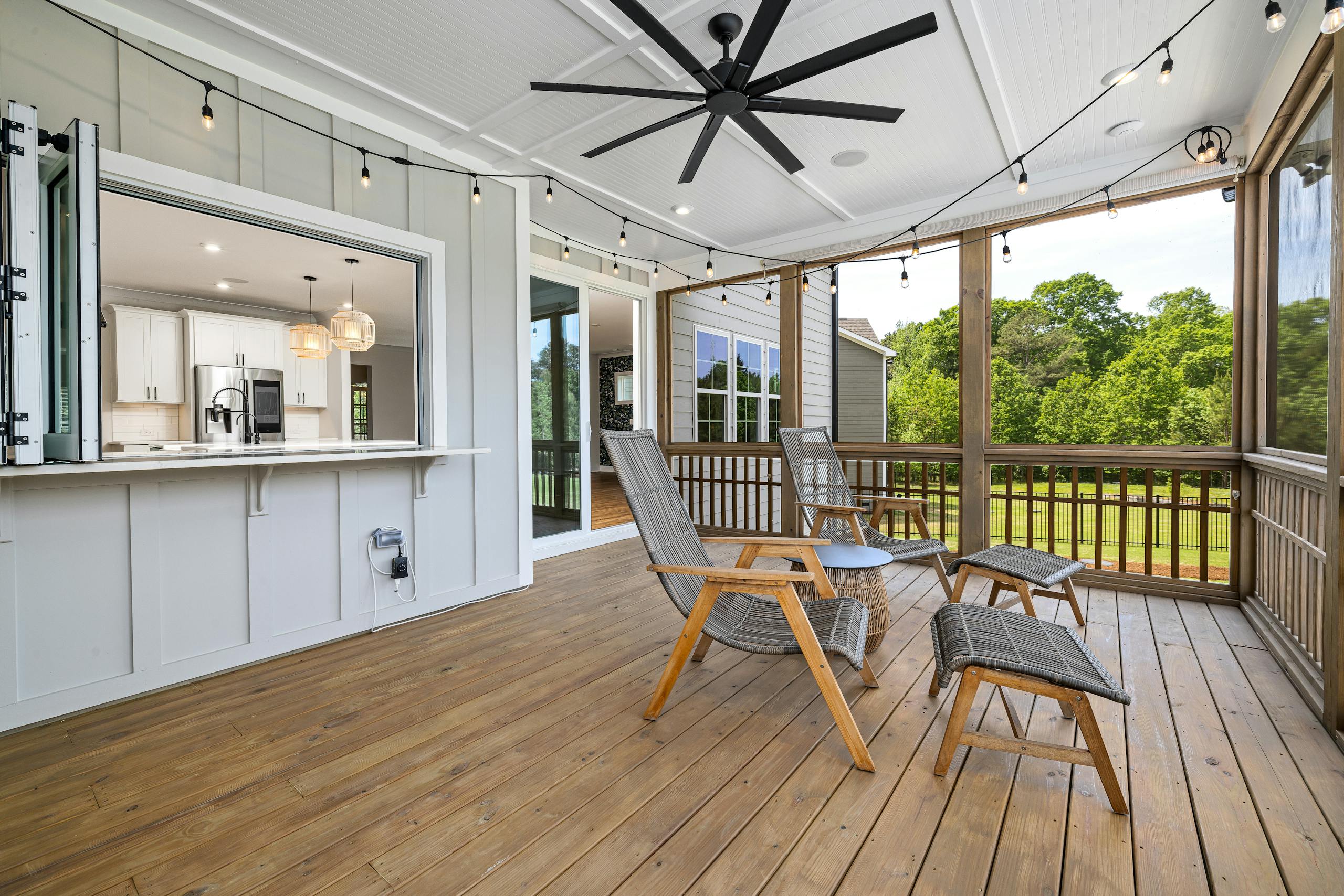 Inviting porch with modern design featuring wooden chairs, ceiling fan, and scenic view.