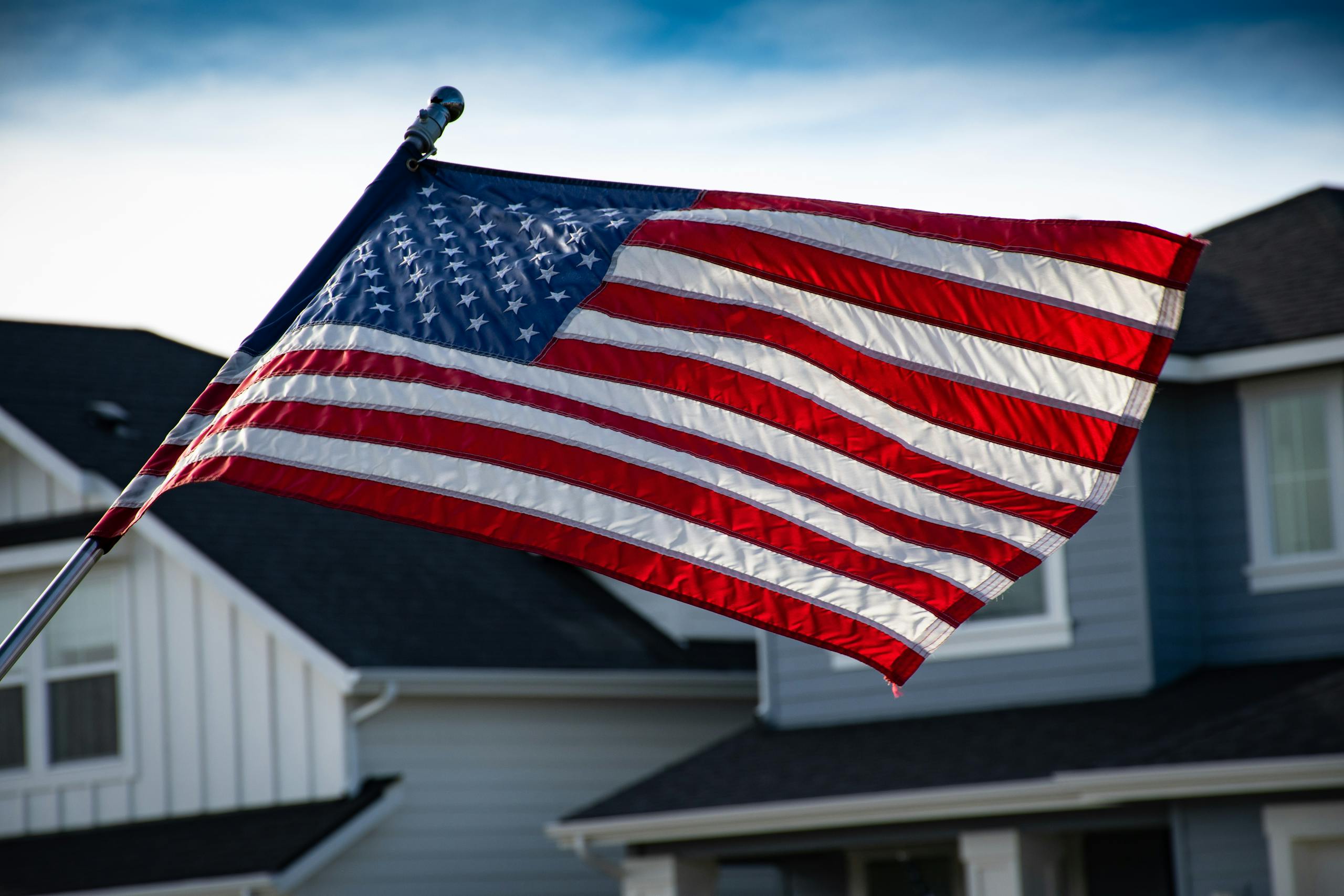 A close-up of the American flag waving in front of a suburban house, symbolizing patriotism.