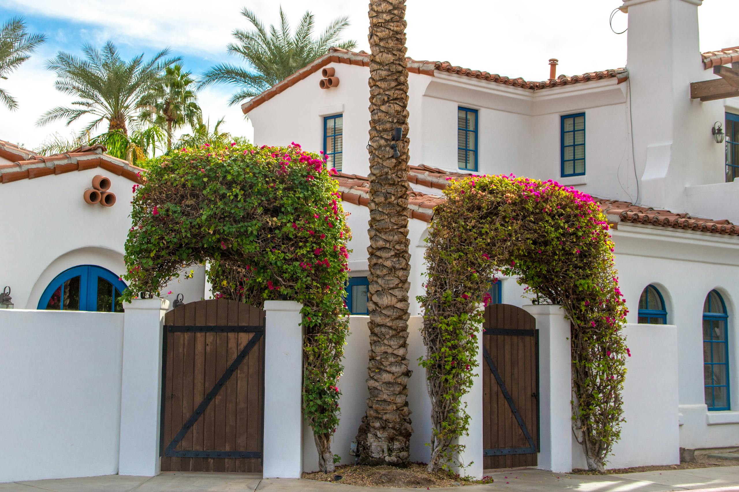 Elegant Mediterranean-style white villa with wooden doors and lush greenery in La Quinta, California.