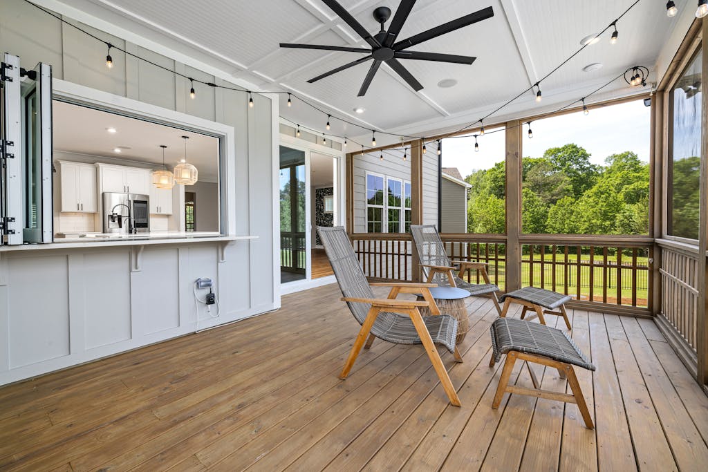 Inviting porch with modern design featuring wooden chairs, ceiling fan, and scenic view.