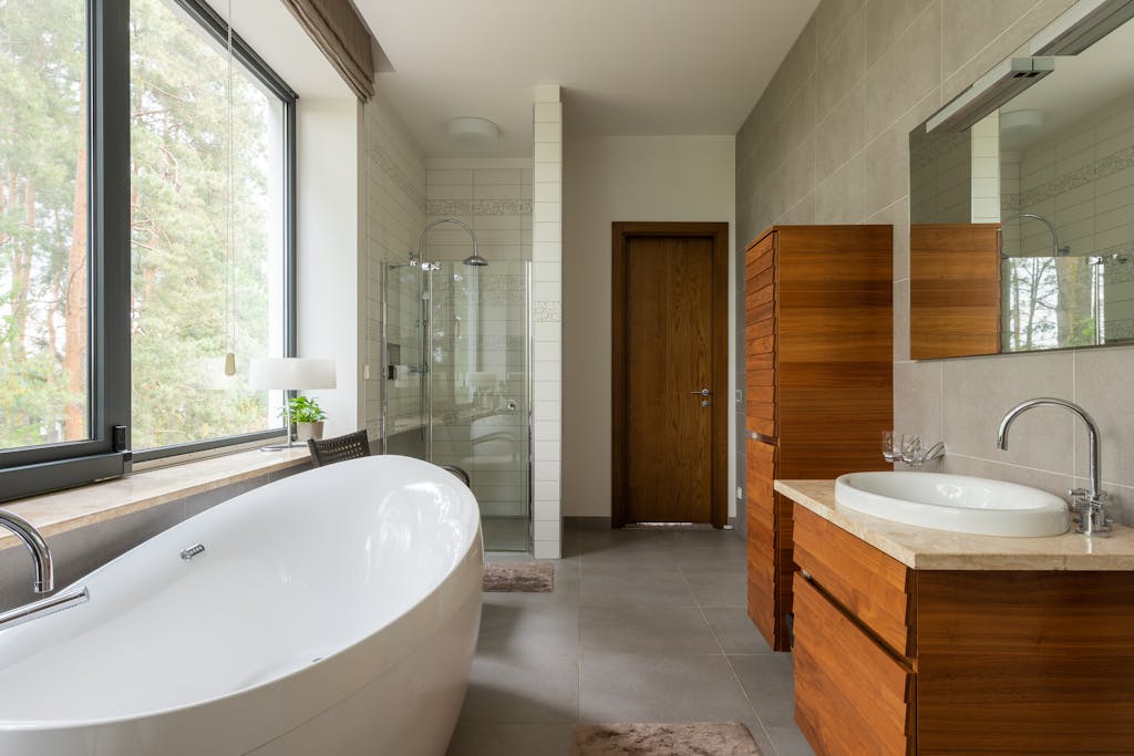 Spacious bathroom featuring a sleek bathtub, wooden vanity, and large window with outdoor view.