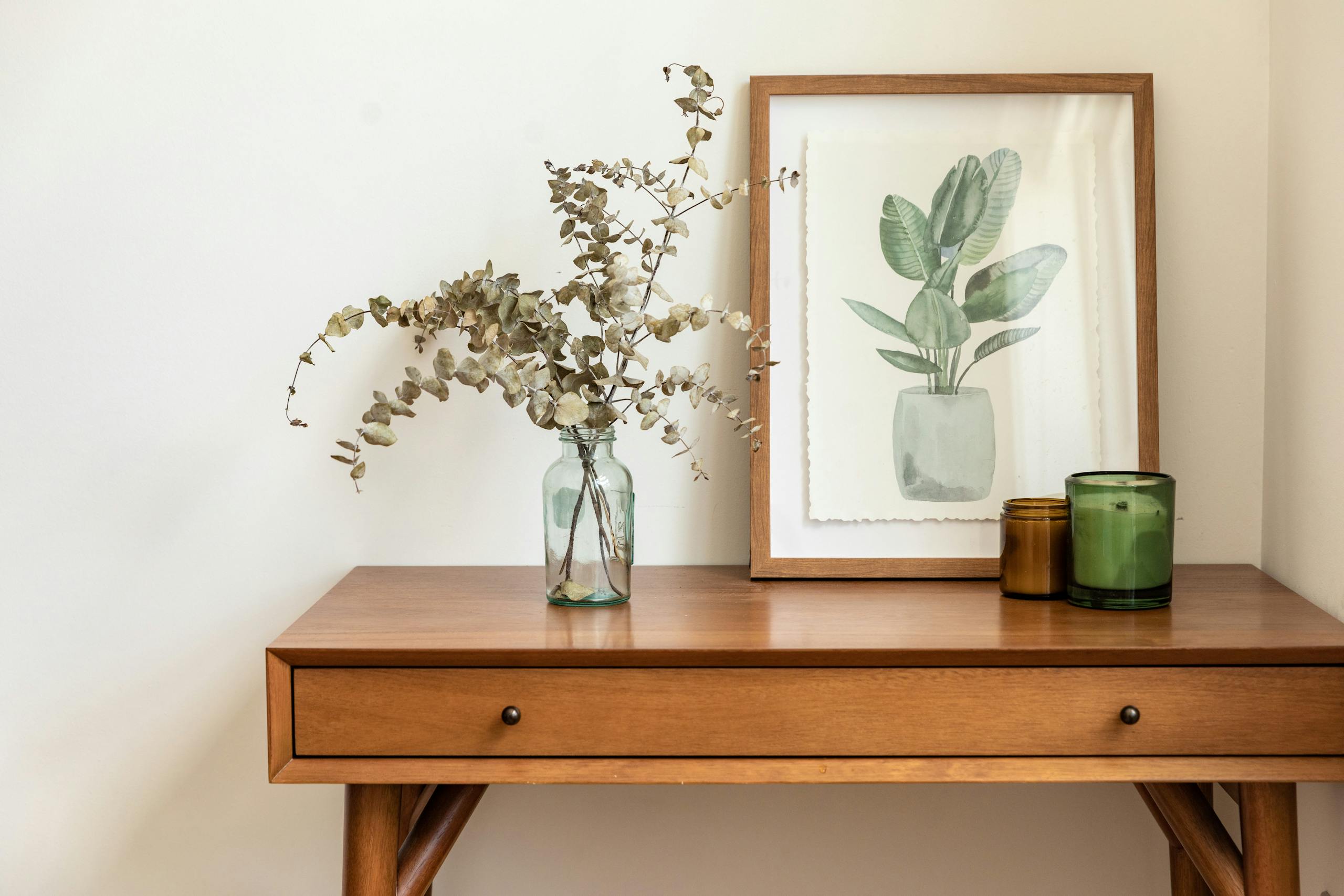 Stylish wooden table featuring dried eucalyptus in a vase and plant artwork. Perfect for modern interiors.